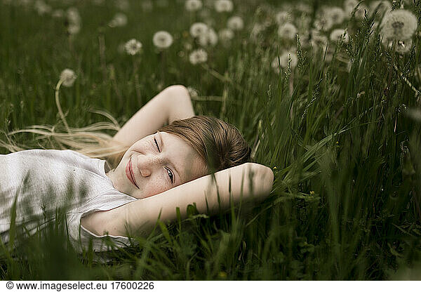 Cute girl winking and lying on dandelions in field