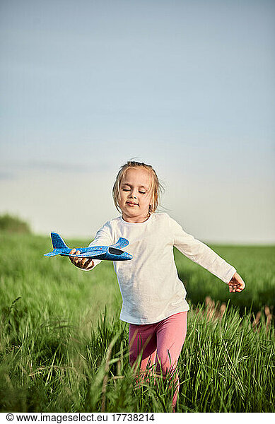 Cute girl with airplane model running in grassy field
