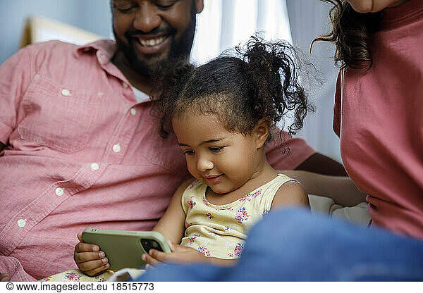 Cute girl with parents watching at smart phone at home