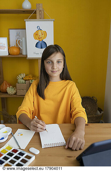 Cute girl with sketch pad sitting at table