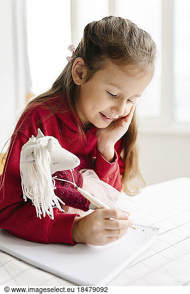 Cute girl with toy doing homework at home