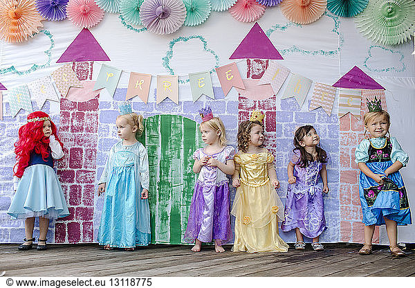 Cute girls standing against castle painting during princess party
