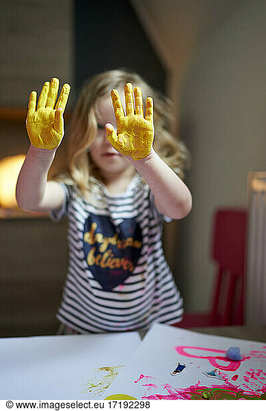 Cute little artist girl showing yellow painted palms to the camera with mother a side.