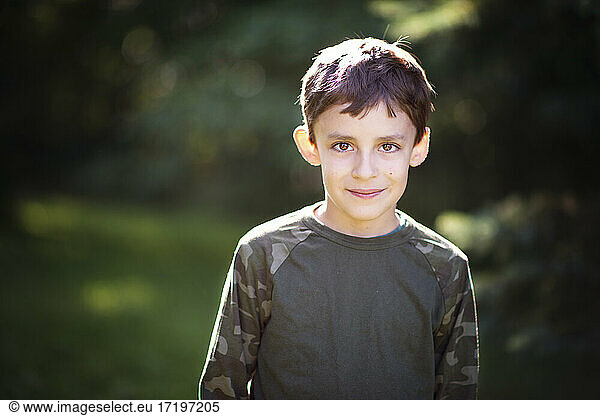 Cute little boy in camo shirt with big brown eyes outdoors.
