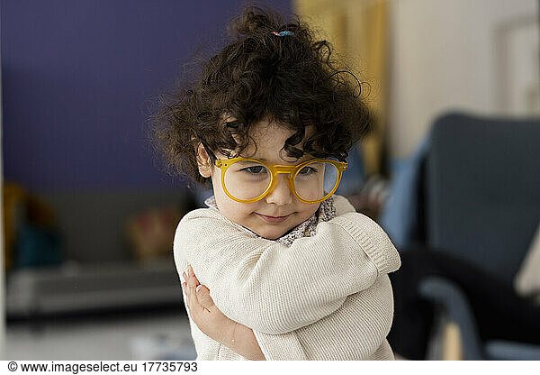 Cute little girl wearing oversized eyeglasses hugging self
