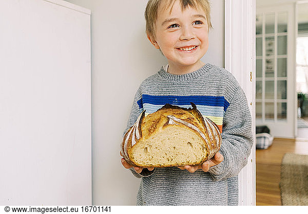 Cute little preschooler holding a homemade loaf of sourdough bread.