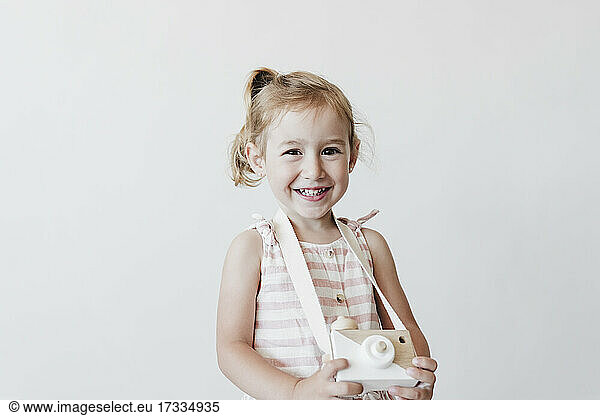 Cute smiling girl holding toy camera against white background