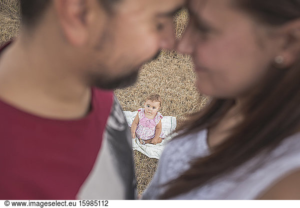 Cute toddler girl seen through parents standing face to face in forest