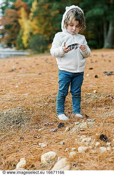 Cute toddler playing with a feather by a lake