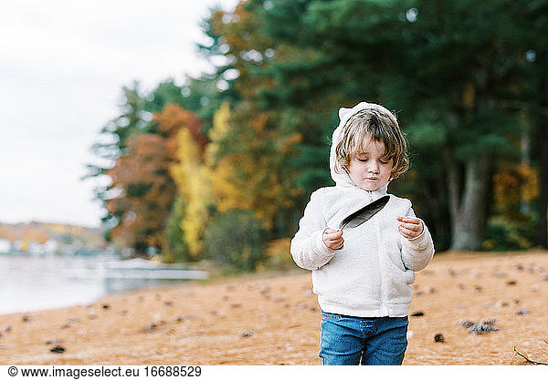 Cute toddler playing with a feather she found by a lake