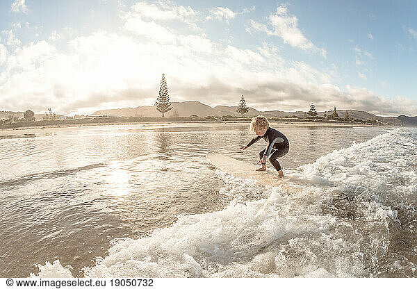 Cute toddler surfing on a wave at a beach in New Zealand
