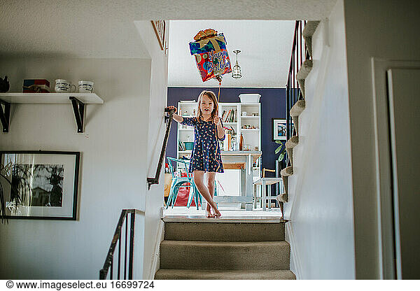 cute young girl standing on stairs with happy birthday balloon