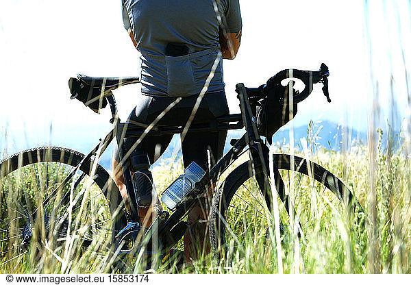 Cyclist leaning on bicycle in a field of grass