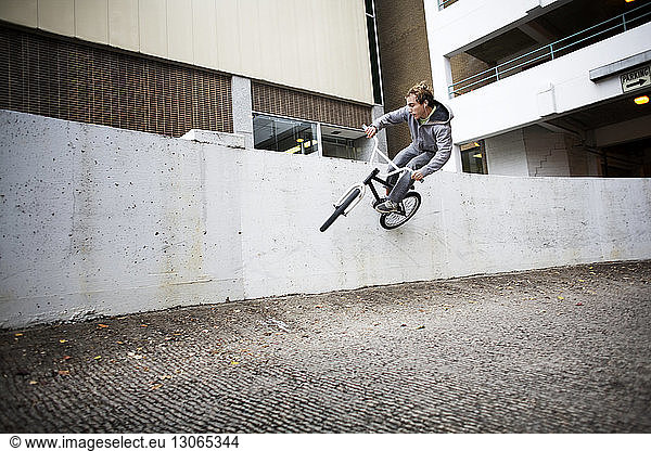 Cyclist performing stunt on retaining wall against building