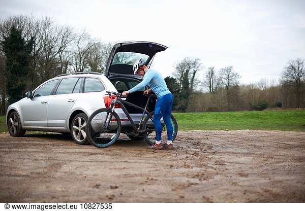 Cyclist wearing bicycle helmet unloading bicycle from car boot