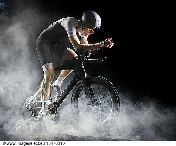 Cyclist wearing sports clothing sitting on turbo trainer against black background