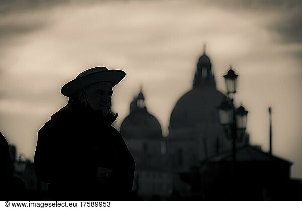 Düstere Stimmung  Gondoliere an Zaun stehend als Schattenriss im Gegenlicht  Kirche Santa Maria della Salute im Hintergrund  Venedig  Venetien  Italien  Europa