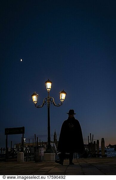 Düstere Stimmung  Mann mit Hut als Schattenriss bei blauer Stunde vor beleuchteter Straßenlaterne  Venedig  Venetien  Italien  Europa
