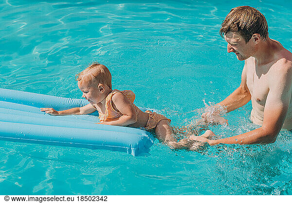 Dad and baby daughter swim on an inflatable mattress in the outd