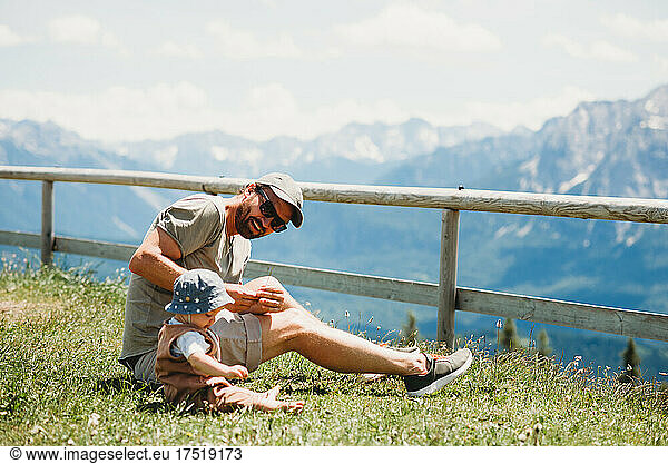 Dad and baby sitting on grass in Alps mountains in summer
