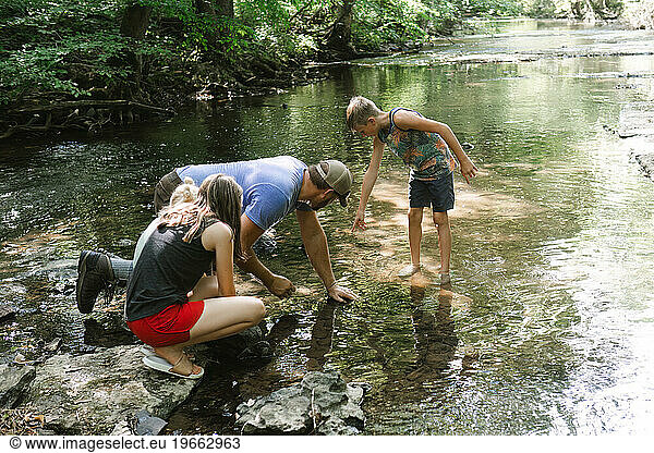 Dad crouching down exploring stream with children on summer day