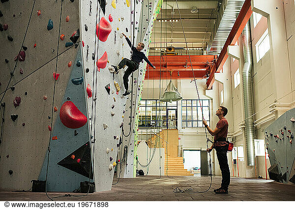 dad helping his son climb an indoor climbing wall