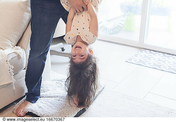 Dad holding daughter upside down in the living room.