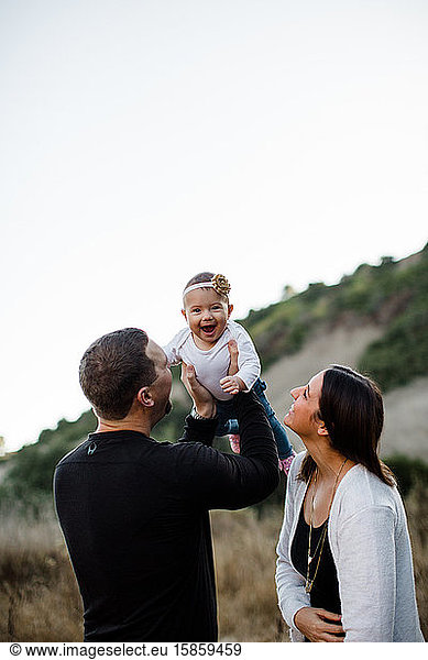 Dad Lifting Infant Daughter as Baby Laughs and Mom Watches