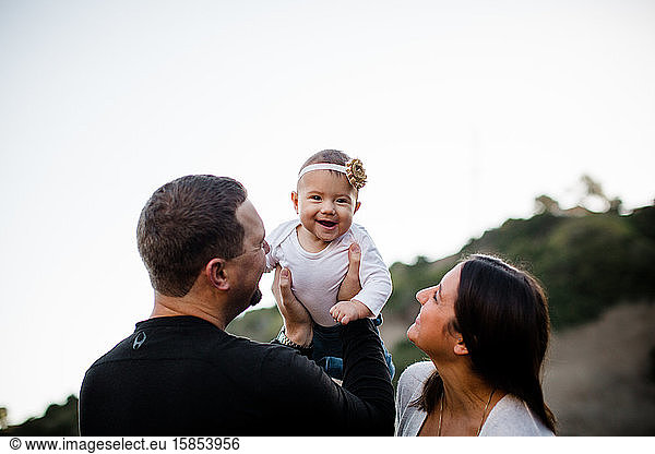 Dad Lifting Infant Daughter as Baby Laughs & Mom Watches