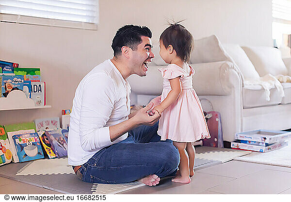 Dad sitting on floor in the living room smiling at baby daughter
