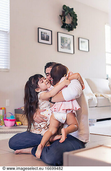 Dad sitting on the living room floor holding both daughters