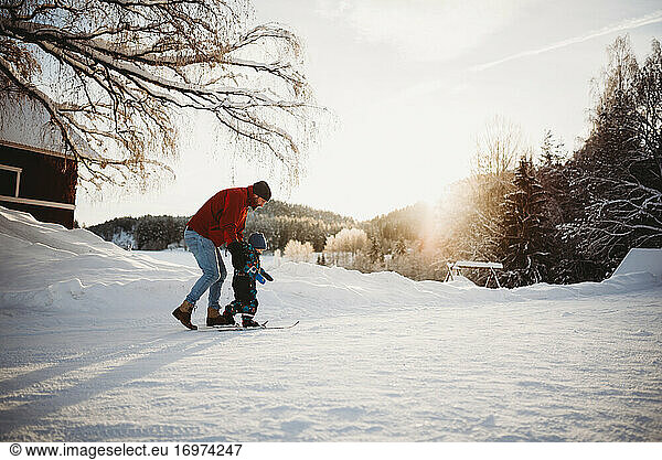 Dad teaching son to cross country ski in farm winter wonderland Norway
