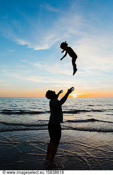 dad throws his toddler daughter into the air at florida beach sunset