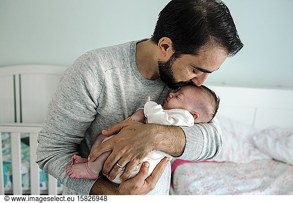 Dad with beard and closed eeditorial kisses head of newborn child