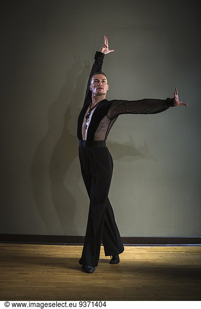 Dancer in dance studio. A man with one arm stretched out and one arm raised.
