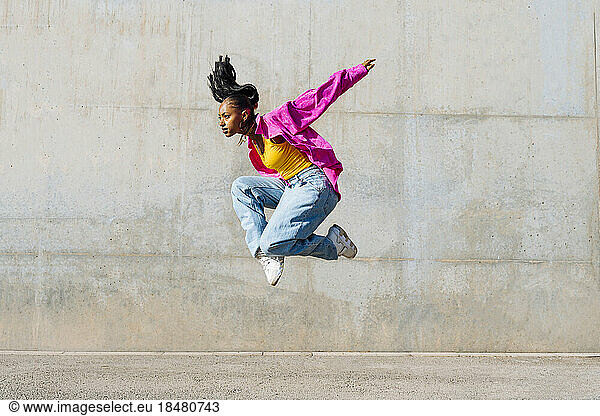 Dancer jumping in front of wall on sunny day