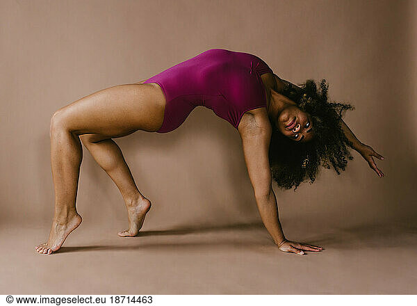 Dancer reaching backwards in backbend on brown backdrop