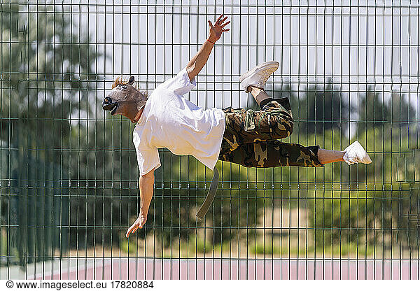 Dancer wearing animal mask flipping in front of fence on sunny day