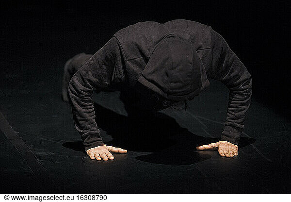 Dancer wearing black hood crouching on stage