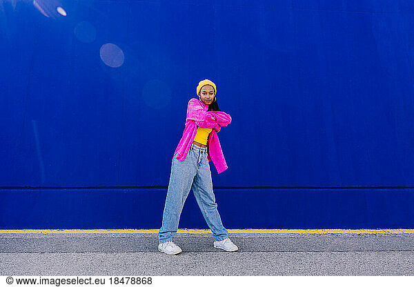 Dancer with arms crossed standing in front of blue wall