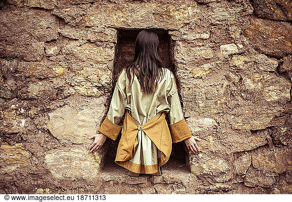 dancer with high fashion jackets sits in key hole in stone wall