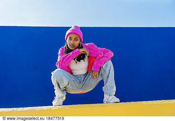 Dancer with knit hat in squatting position on wall