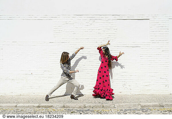 Dancers performing flamenco in front of white wall on sunny day