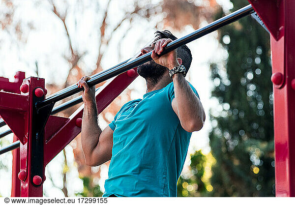 Dark-haired athlete with beard doing a pull-up on a calisthenics bar. Outdoor crossfit concept.