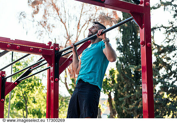 Dark-haired athlete with beard doing a pull-up on a calisthenics bar. Outdoor crossfit concept.
