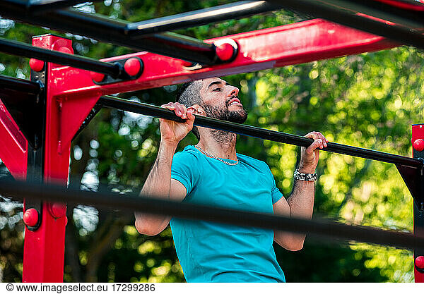 Dark-haired athlete with beard doing a pull-up on a calisthenics bar. View between bars. Outdoor crossfit concept.