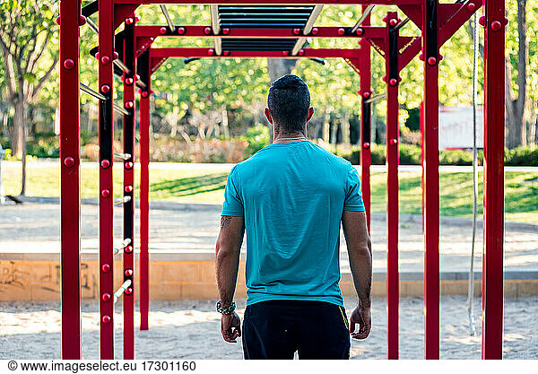 Dark-haired athlete with beard ready to train on calisthenics bars. Rear view.