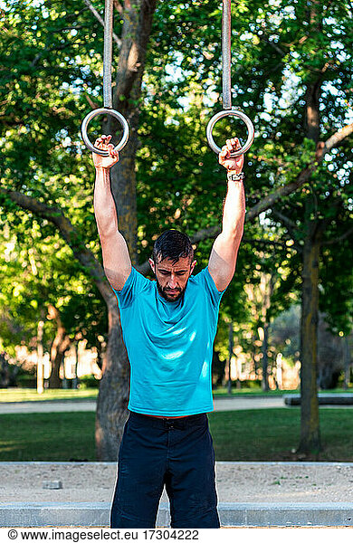 Dark-haired athlete with beard ready to use the gymnastic rings.