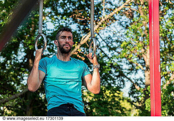 Dark-haired athlete with beard training on gymnastic rings.