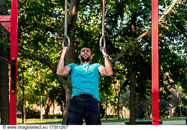 Dark-haired athlete with beard training on gymnastic rings.